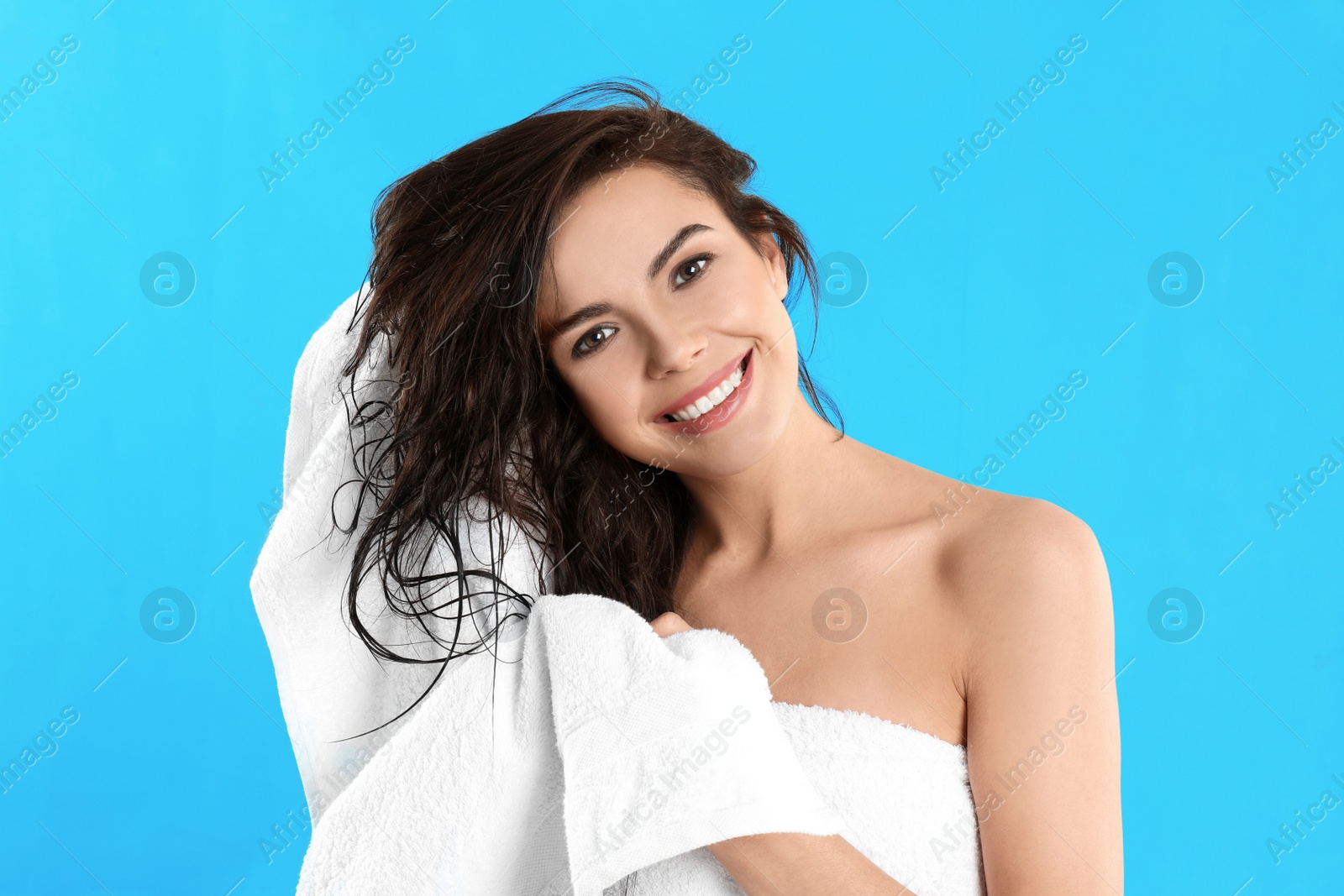 Photo of Young woman drying hair with towel on light blue background