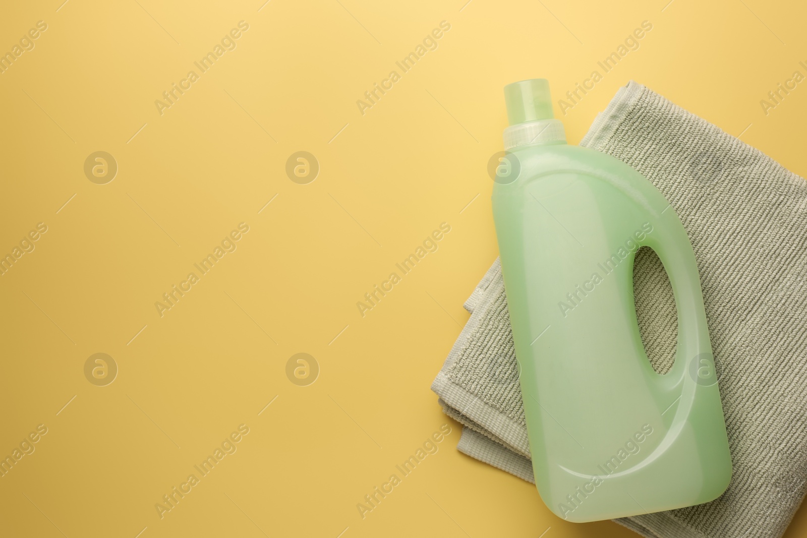 Bottle of fabric softener and towel on pale yellow background, top view. Space for text Photo of Bottle of fabric softener and towel on pale yellow background, top view. Space for text