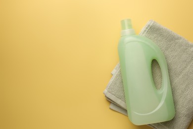Photo of Bottle of fabric softener and towel on pale yellow background, top view. Space for text