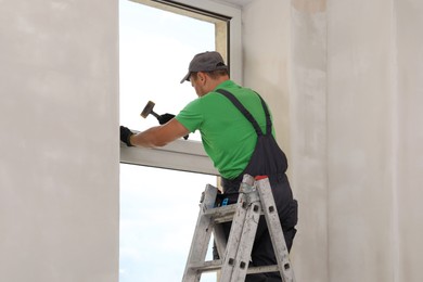 Worker in uniform using hammer for window installation indoors