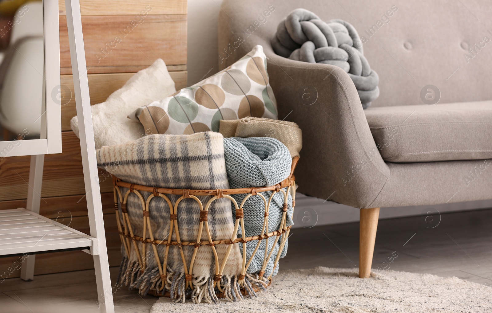 Photo of Basket with blankets and pillows near sofa indoors