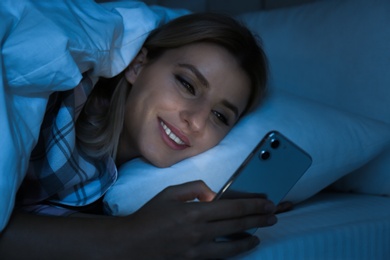 Photo of Young woman using smartphone in bed at night. Nomophobia and sleeping disorder problem