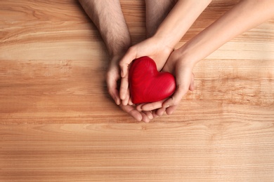Photo of Couple holding decorative heart on wooden background, top view