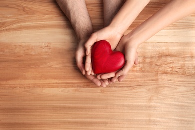 Couple holding decorative heart on wooden background, top view