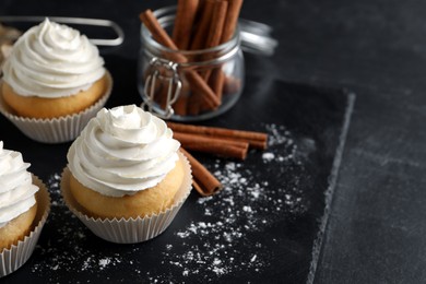 Photo of Delicious cupcakes with cream and cinnamon on black table. Space for text