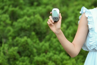 Photo of Woman holding digital glucometer on blurred background. Diabetes control