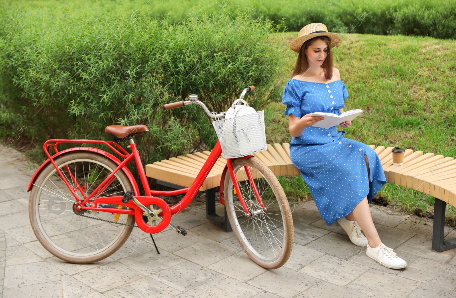 Photo of Young pretty woman reading on bench near bicycle in park