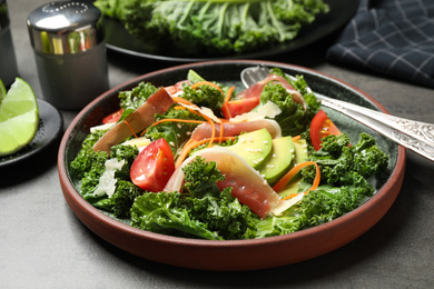 Photo of Delicious kale salad with prosciutto served on grey table