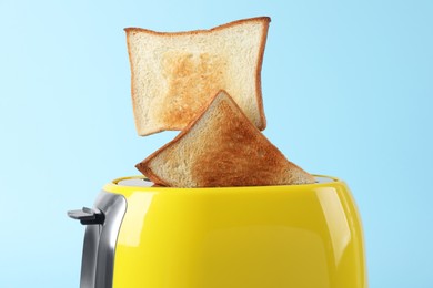 Photo of Bread slices popping up from modern toaster on light blue background, closeup