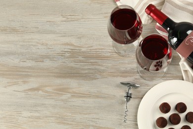 Photo of Glasses and bottle of red wine with chocolate candies on white wooden table, flat lay. Space for text