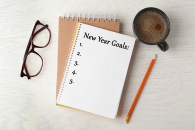 Image of Notebook with inscription New Year Goals, cup of coffee, glasses and pencil on white wooden table, flat lay