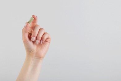 Photo of Woman holding vitamin capsule on grey background, closeup with space for text. Health supplement