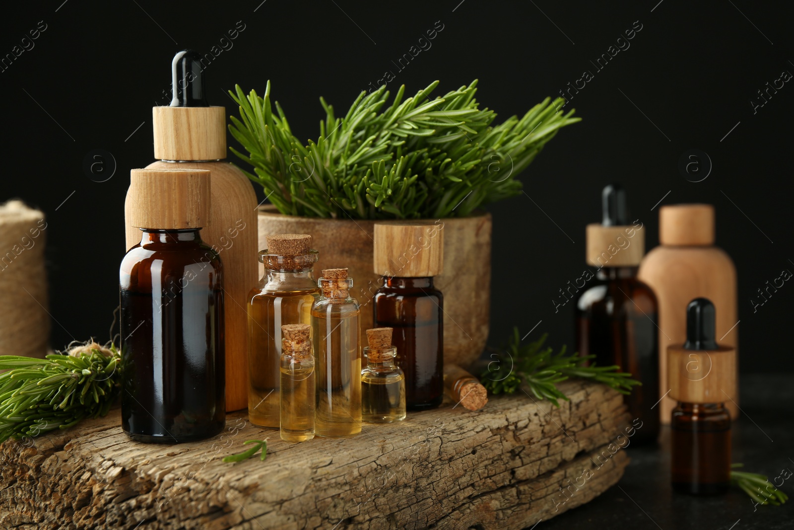 Photo of Essential oils in bottles, rosemary and wood on table against black background, closeup