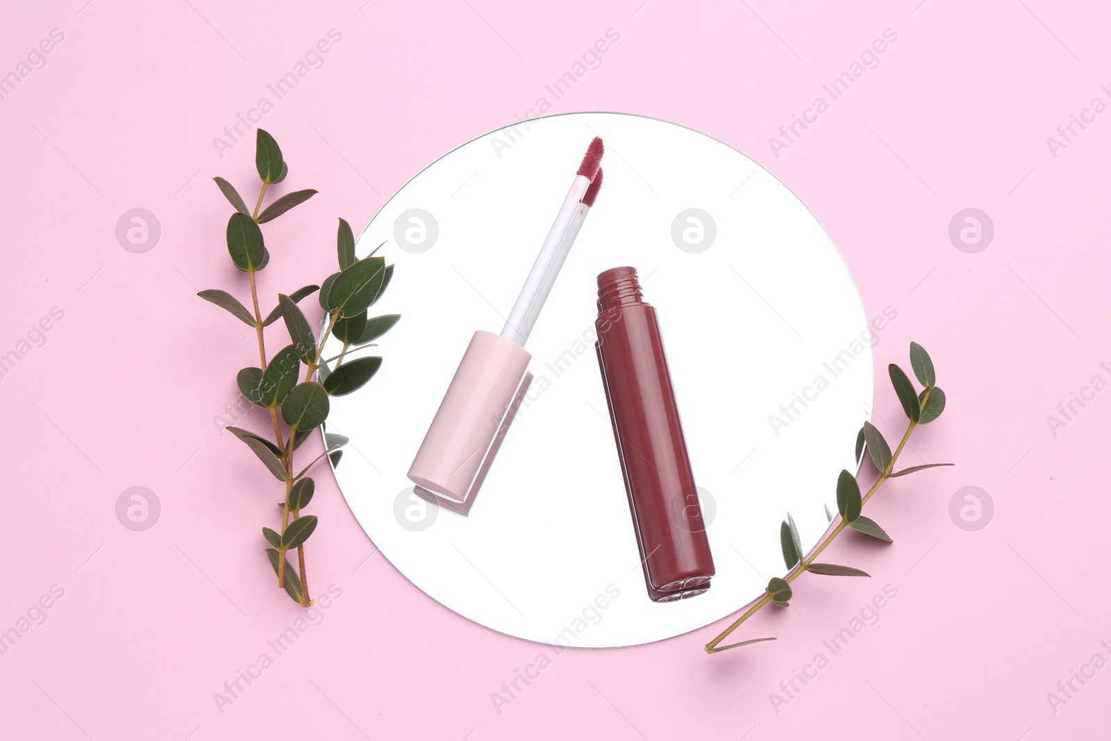 Photo of Lip gloss, green twigs and mirror on pink background, flat lay