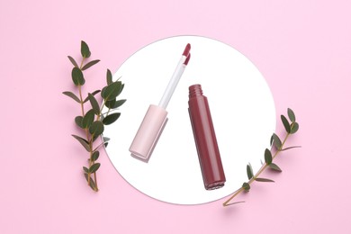 Photo of Lip gloss, green twigs and mirror on pink background, flat lay