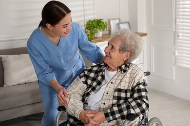 Photo of Young caregiver assisting senior woman in wheelchair indoors. Home health care service