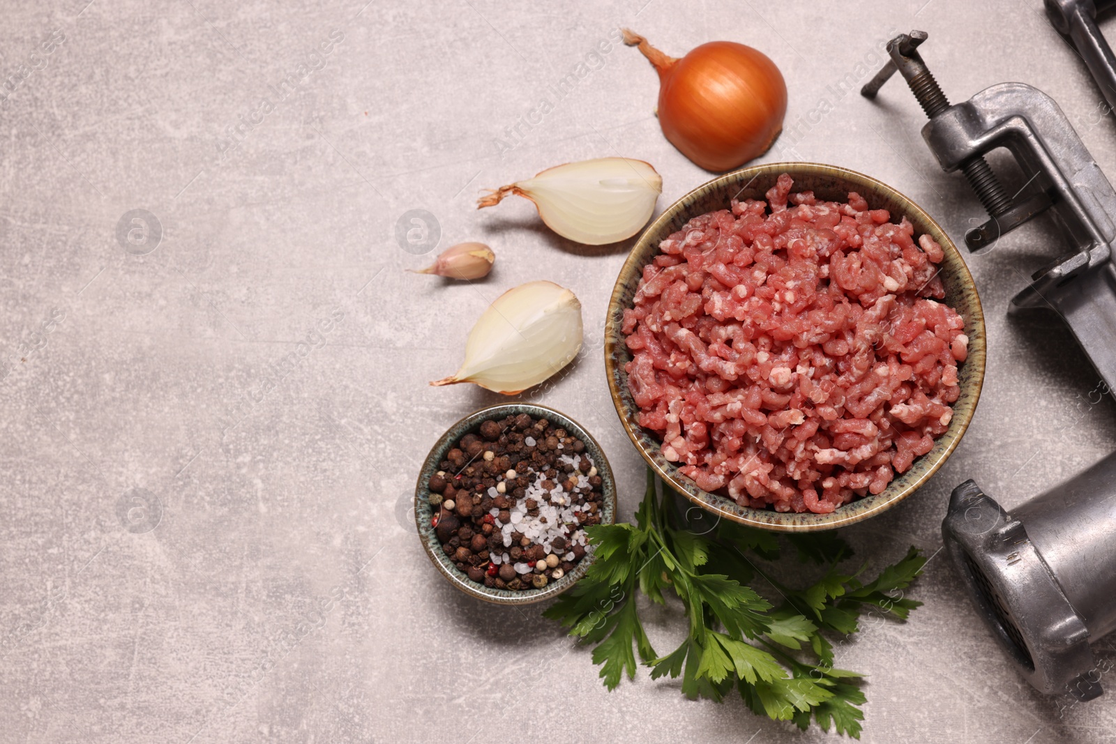 Photo of Manual meat grinder with beef mince, peppercorns, onion and parsley on light grey table, flat lay. Space for text