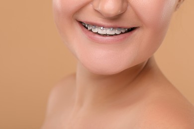 Photo of Happy woman with dental braces on brown background, closeup