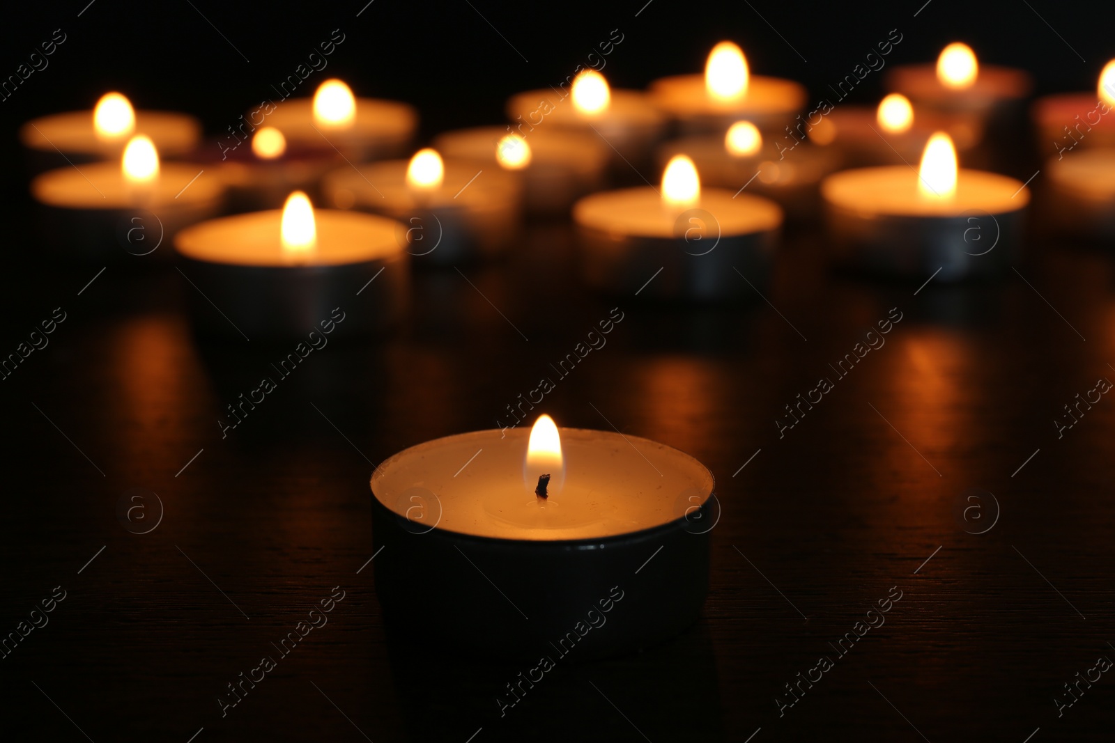 Photo of Many burning candles on wooden table in darkness, closeup. Space for text