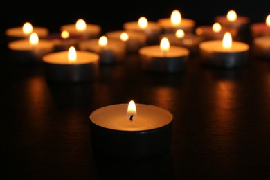 Many burning candles on wooden table in darkness, closeup. Space for text