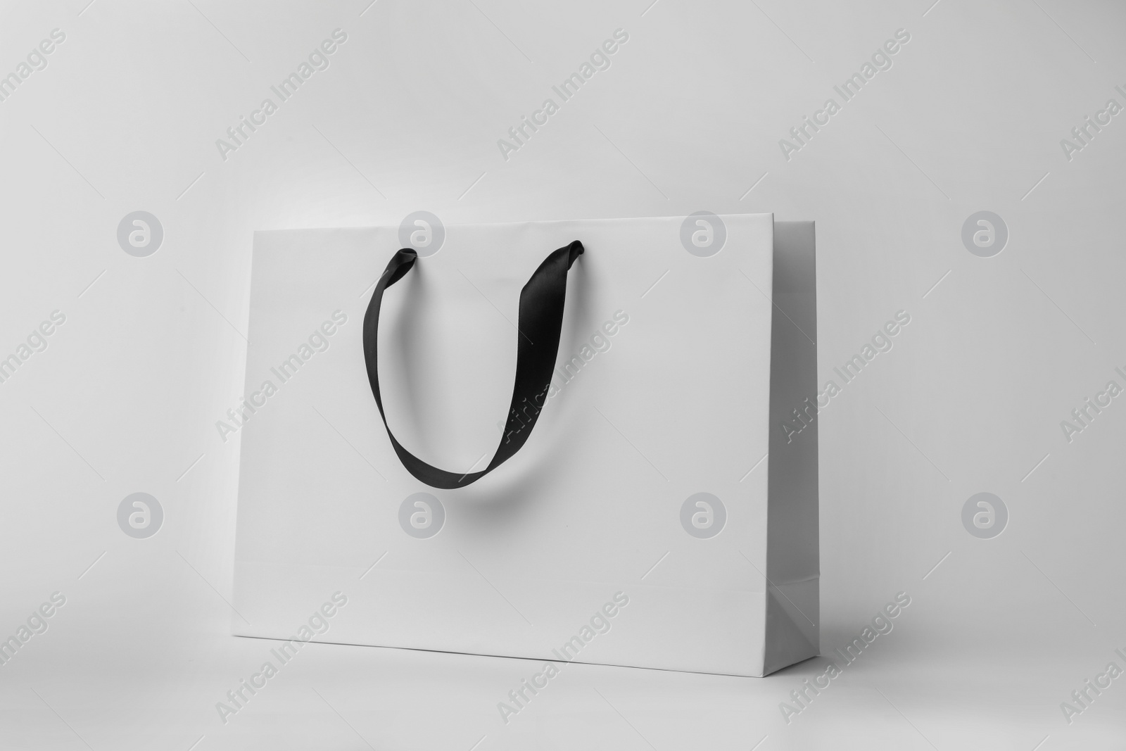 Photo of Paper shopping bag with ribbon handles on white background. Mockup for design