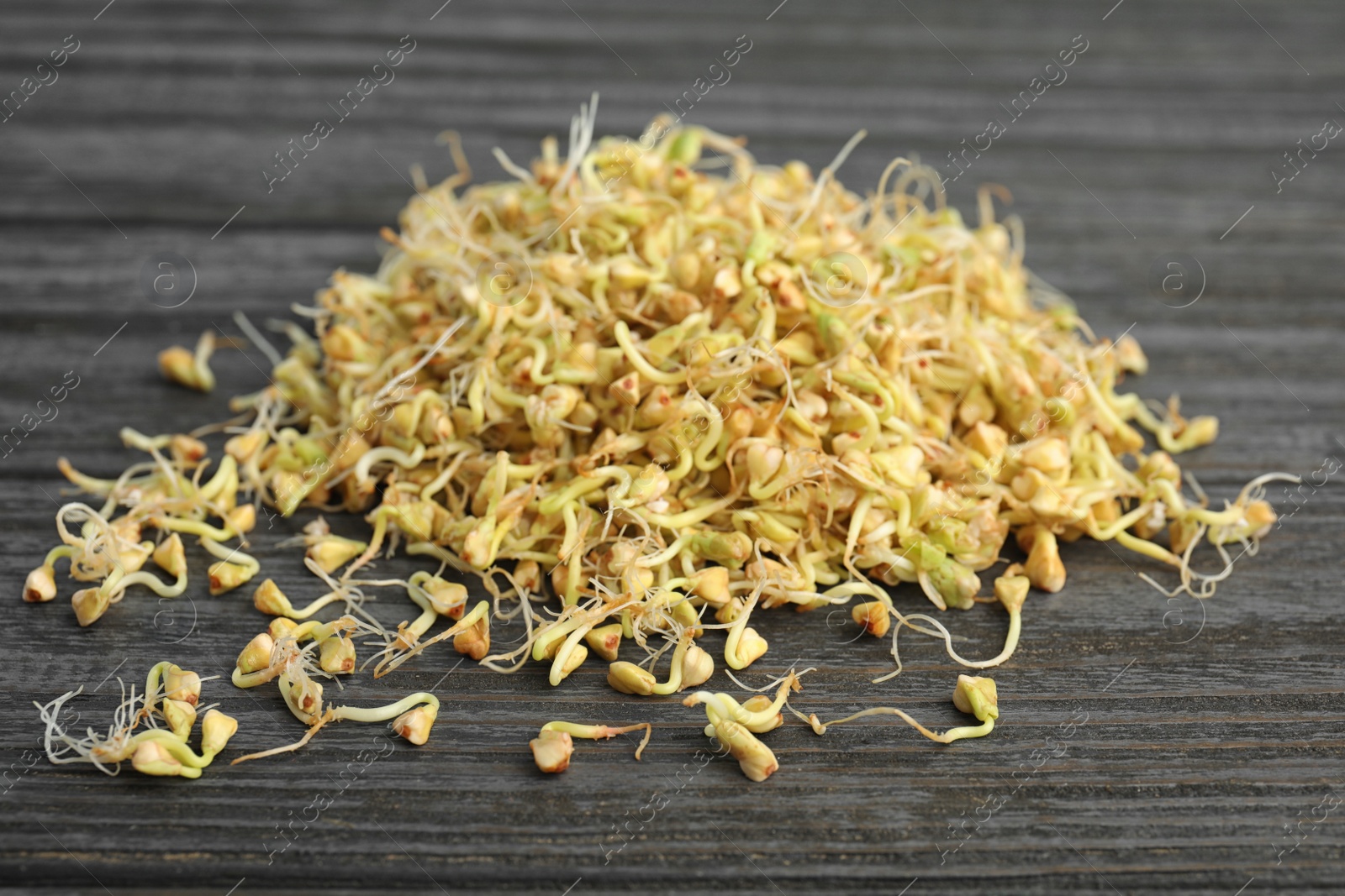 Photo of Pile of sprouted green buckwheat on dark wooden table, closeup