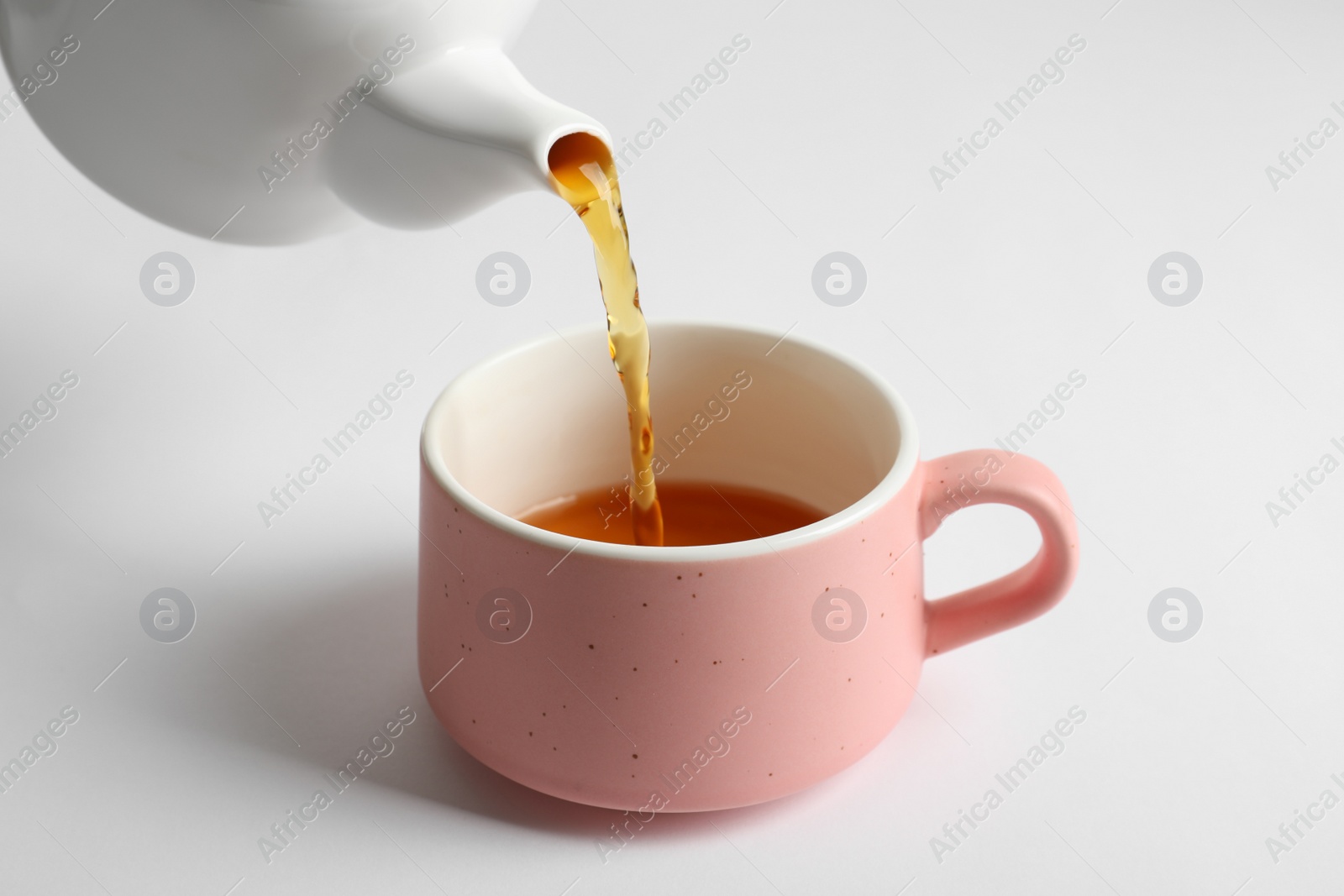 Photo of Pouring hot tea into ceramic cup on white background