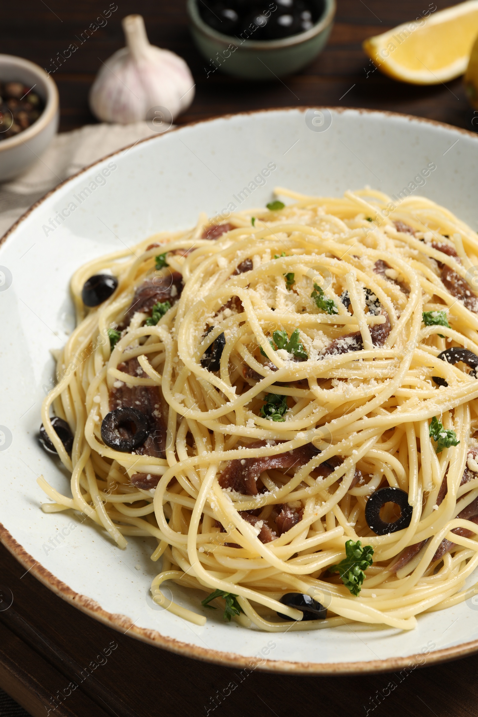 Photo of Delicious pasta with anchovies, olives and parmesan cheese on wooden table, closeup