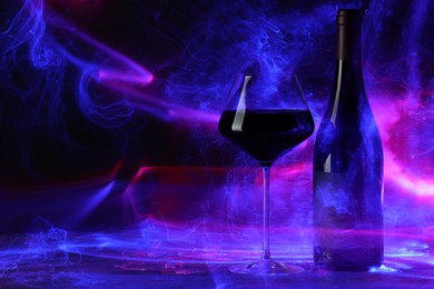 Photo of Red wine in glass and bottle in neon lights, space for text