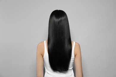 Photo of Young woman with long straight hair on grey background, back view