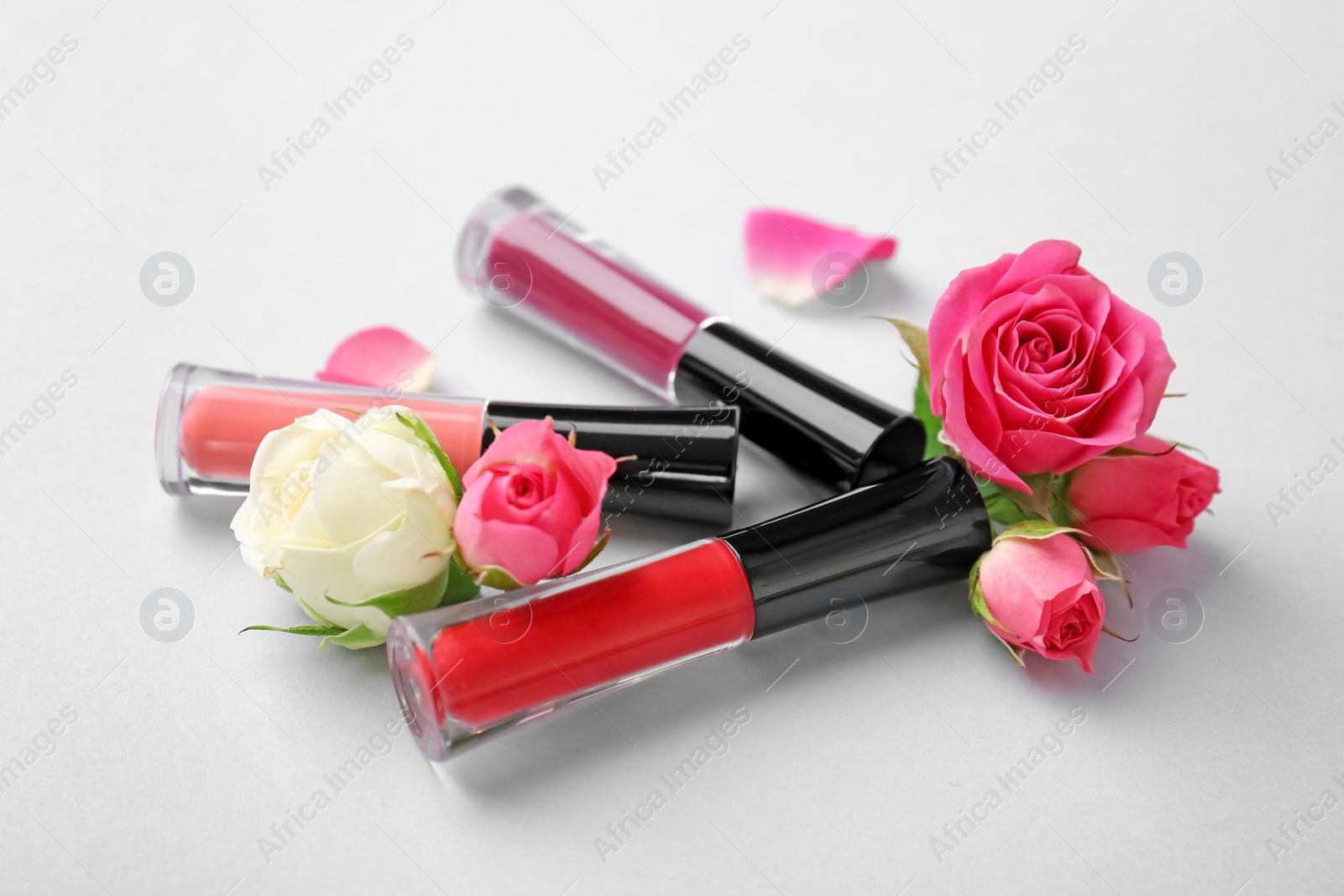 Photo of Lip glosses and flowers on light background