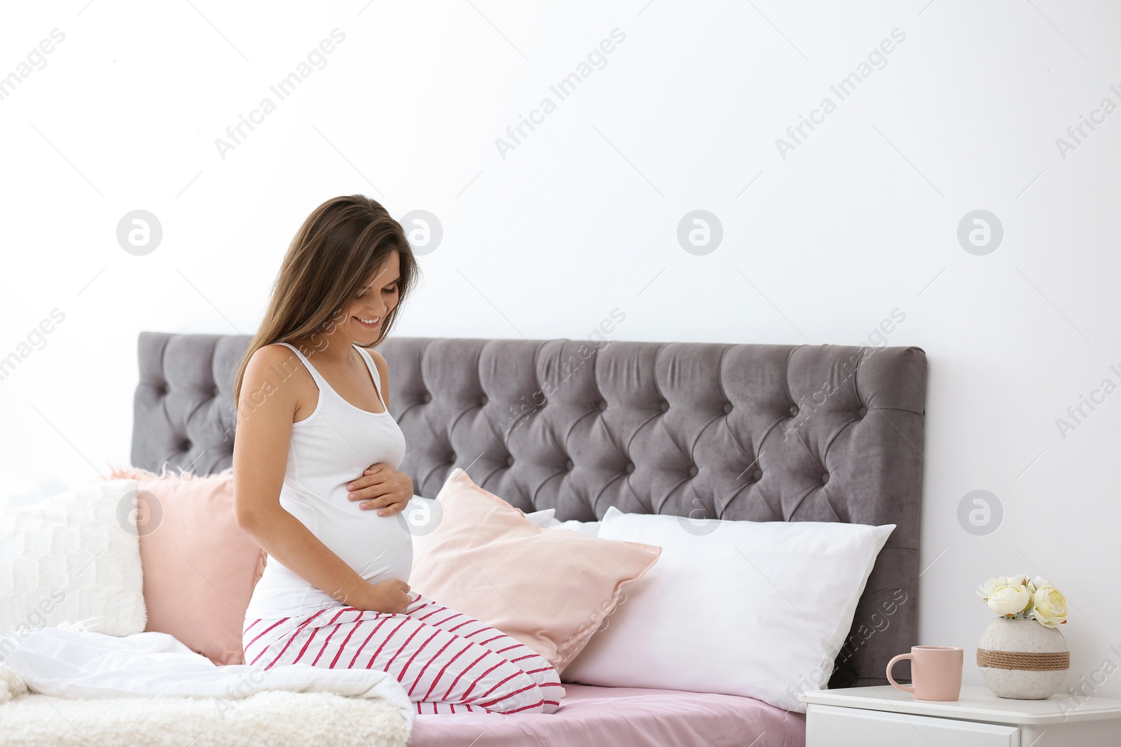 Photo of Happy pregnant woman sitting on bed at home