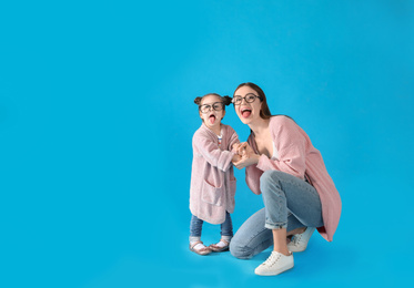 Young mother and little daughter with glasses on blue background