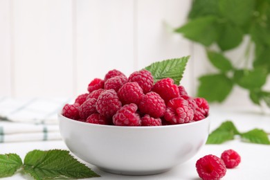 Photo of Bowl of fresh ripe raspberries with green leaves on white table