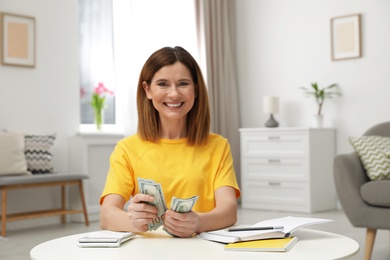 Photo of Smiling woman counting money at table indoors