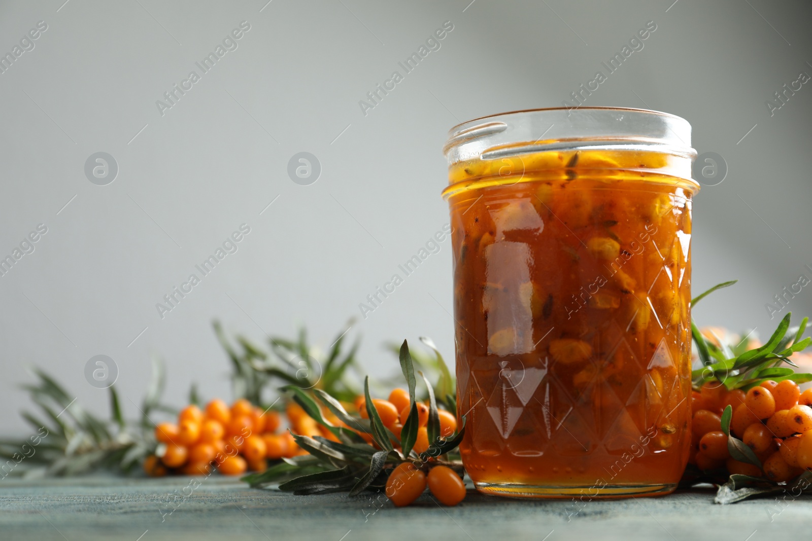 Photo of Delicious sea buckthorn jam and fresh berries on wooden table. Space for text