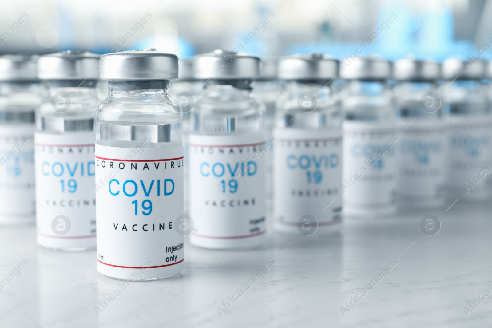 Photo of Glass vials with COVID-19 vaccine on white wooden table