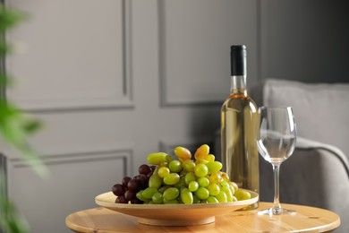 Photo of Bottle of wine, glass and fresh grapes on wooden table indoors