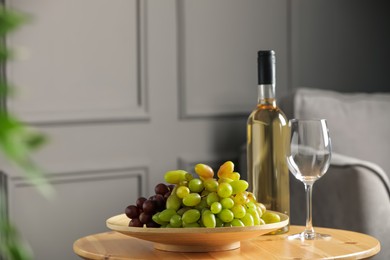 Bottle of wine, glass and fresh grapes on wooden table indoors