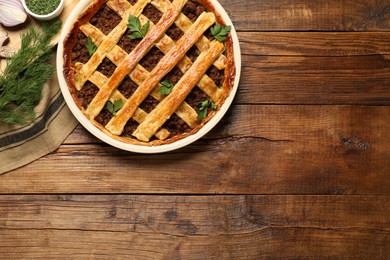 Photo of Freshly baked meat pie and products on wooden table, flat lay. Space for text
