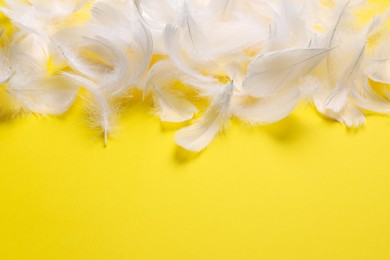 Many fluffy bird feathers on yellow background, flat lay. Space for text