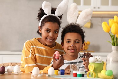 Photo of Happy African American mother and her cute son with Easter eggs at table in kitchen
