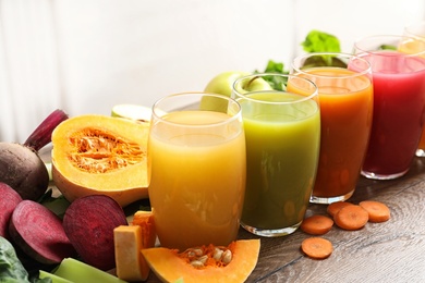 Glasses with different juices and fresh ingredients on wooden table