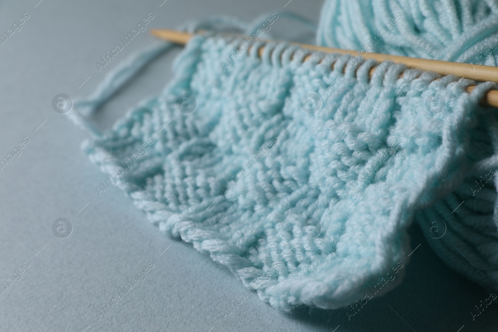 Photo of Soft turquoise knitting and needles on light blue background, closeup