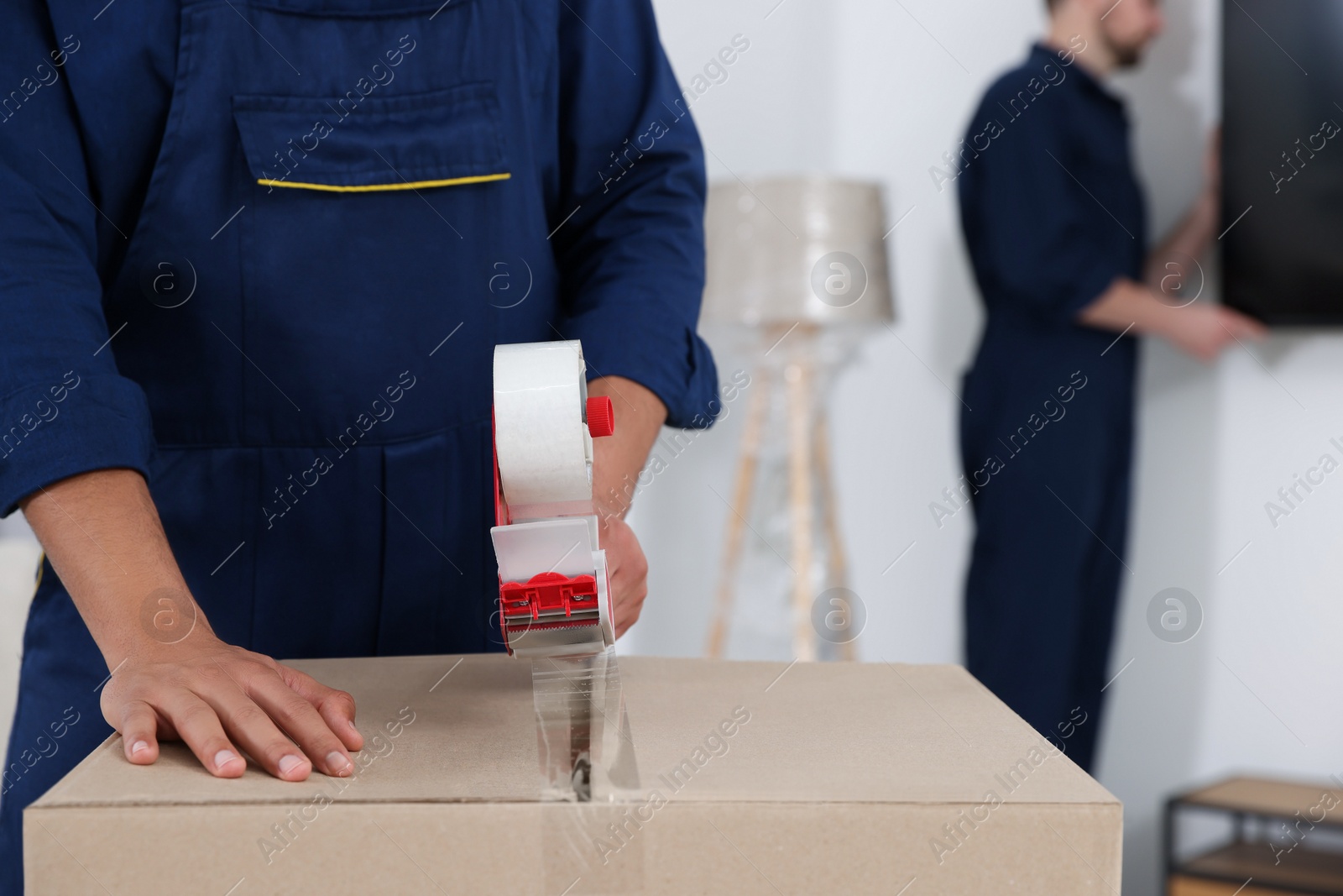 Photo of Male mover packing box with adhesive tape in house, closeup. Space for text