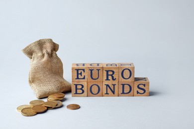 Photo of Word Eurobonds made of wooden cubes with letters and coins on light grey background