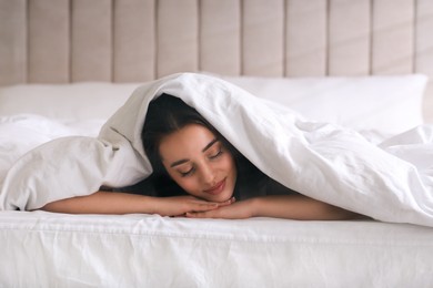 Photo of Young woman covered with warm white blanket sleeping in bed