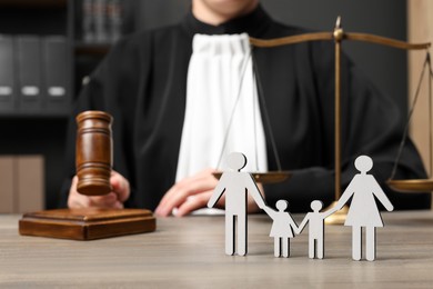 Photo of Family law. Judge with gavel and scales of justice sitting at wooden table, focus on figure of parents and children