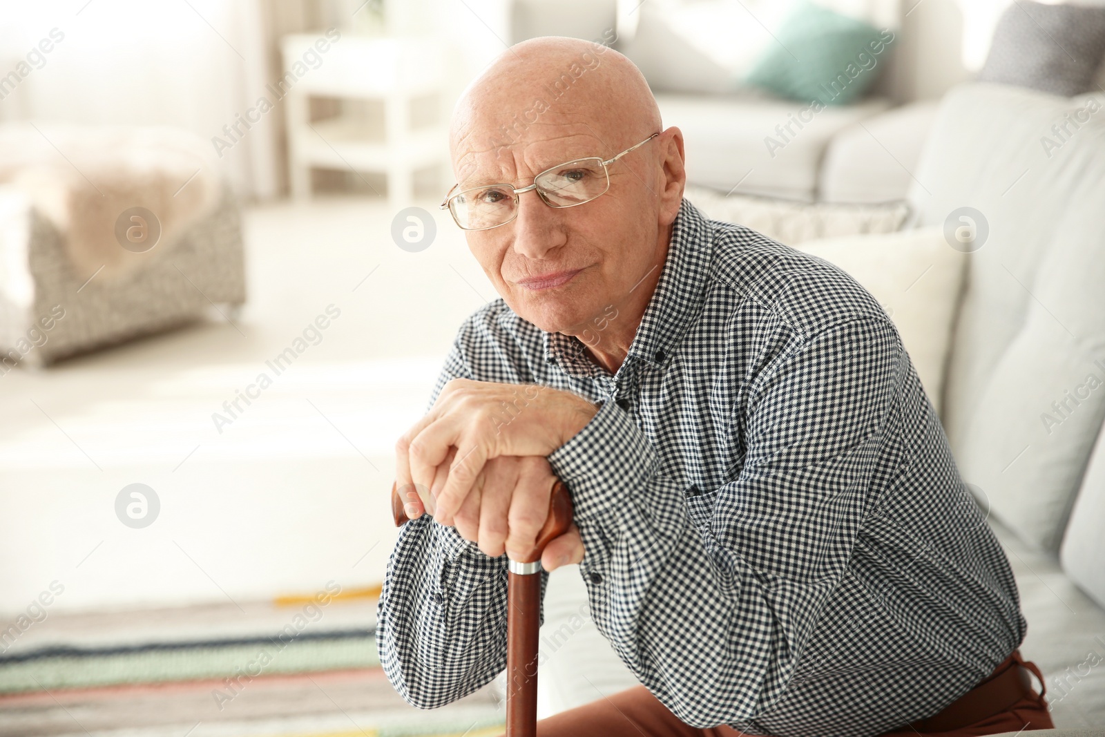 Photo of Elderly man with cane sitting on couch in living room