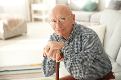 Elderly man with cane sitting on couch in living room